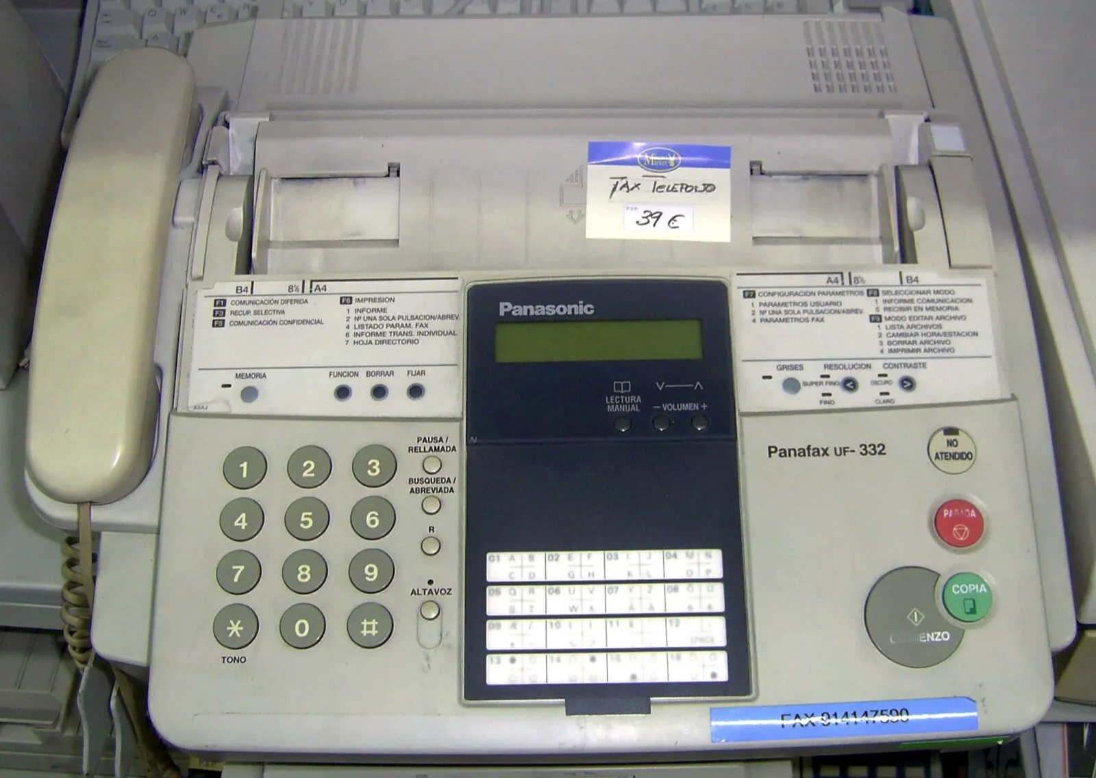 Máquina de fax de oficina, gris, con tubo telefónico a la izquierda, teclado numérico y una pantalla chica.
