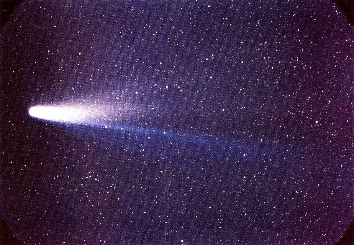 Cometa con la cabeza brillante y una cola azulada que se abre hacia la derecha, sobre un campo de estrellas.