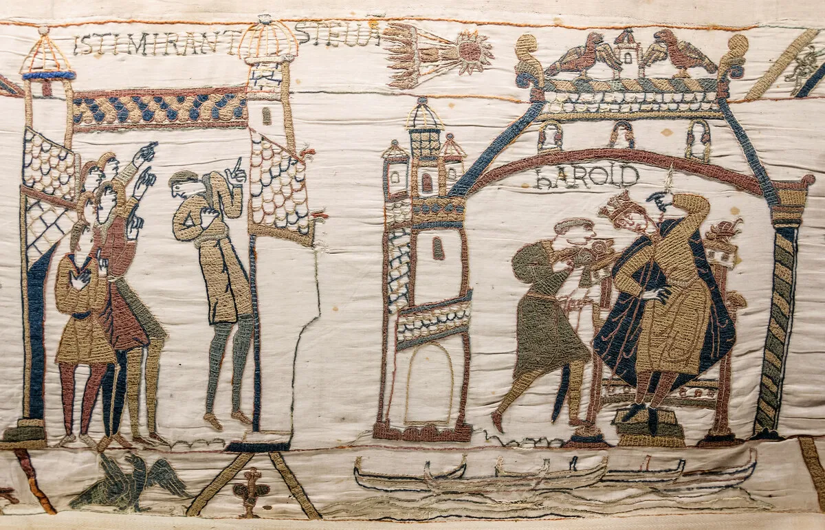 Bordado medieval con figuras que señalan hacia arriba una estrella con cola y, a la derecha, un rey sentado en su trono.