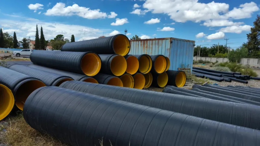 Tramos de tubería negra apilados al aire libre para una obra de acueducto.