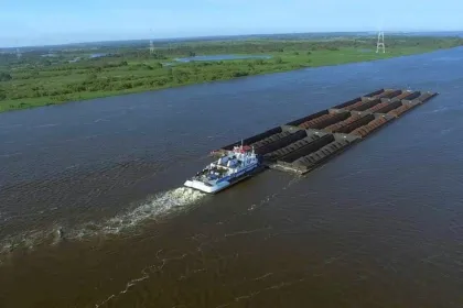 Un remolcador navega con barcazas por un río ancho.