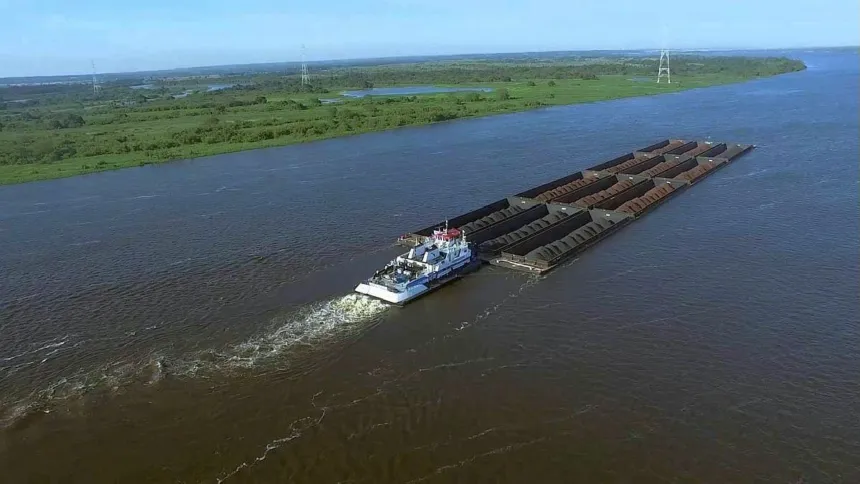 Un remolcador navega con barcazas por un río ancho.