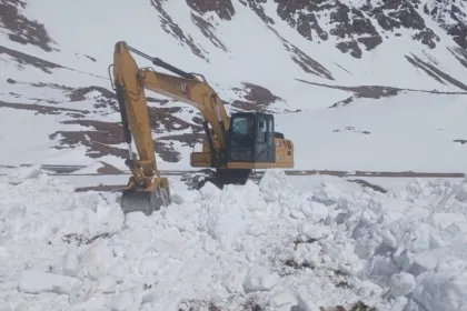 Una excavadora trabaja para despejar nieve en un camino de montaña.