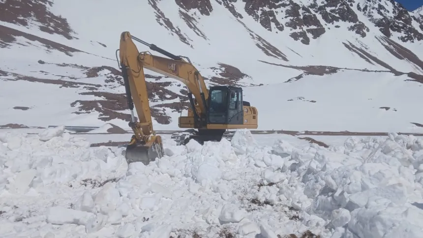 Una excavadora trabaja para despejar nieve en un camino de montaña.