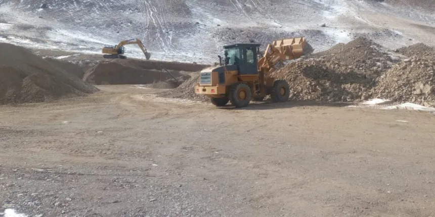 Una cargadora y una excavadora trabajan para despejar un camino de montaña nevado.