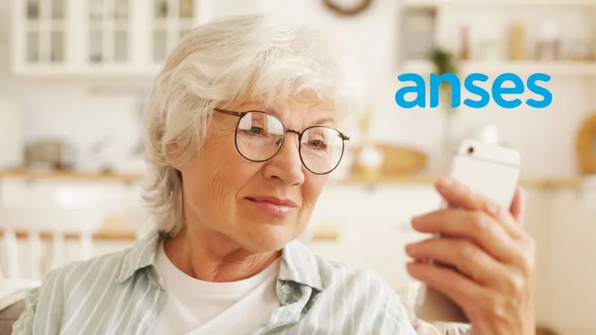 Una mujer mayor mira su celular junto al logo de ANSES.