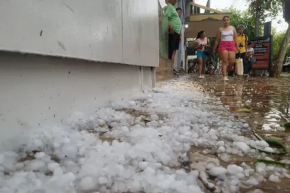 Granizo acumulado sobre una calle mojada mientras varias personas caminan.