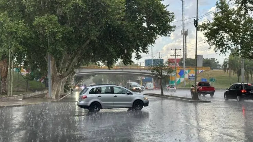 Autos circulan bajo la lluvia intensa por una calle con agua acumulada.