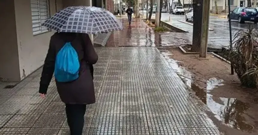 Una persona camina con paraguas por una vereda mojada.