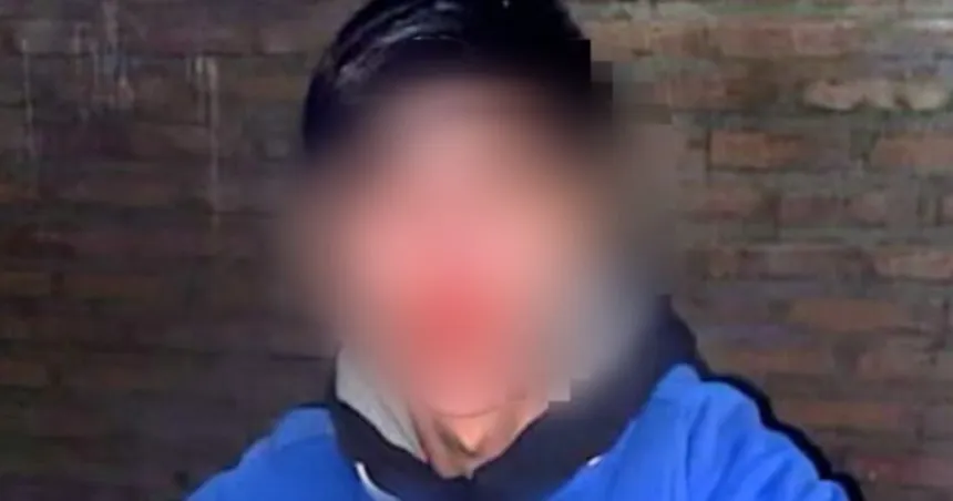 Un joven con buzo azul posa frente a una pared de ladrillos; su rostro está difuminado.