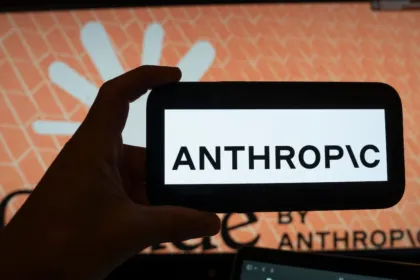 Una mano muestra el nombre Anthropic en un celular frente a una pantalla.
