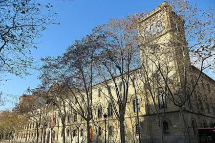 Fachada de un edificio de la Universitat de Barcelona junto a una avenida arbolada.