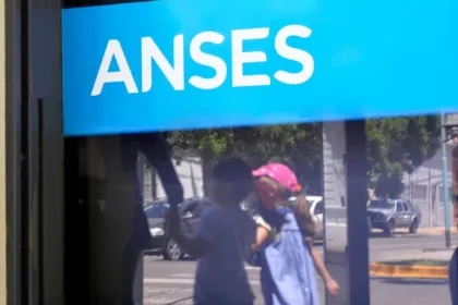 Cartel de ANSES en una vidriera con personas reflejadas.