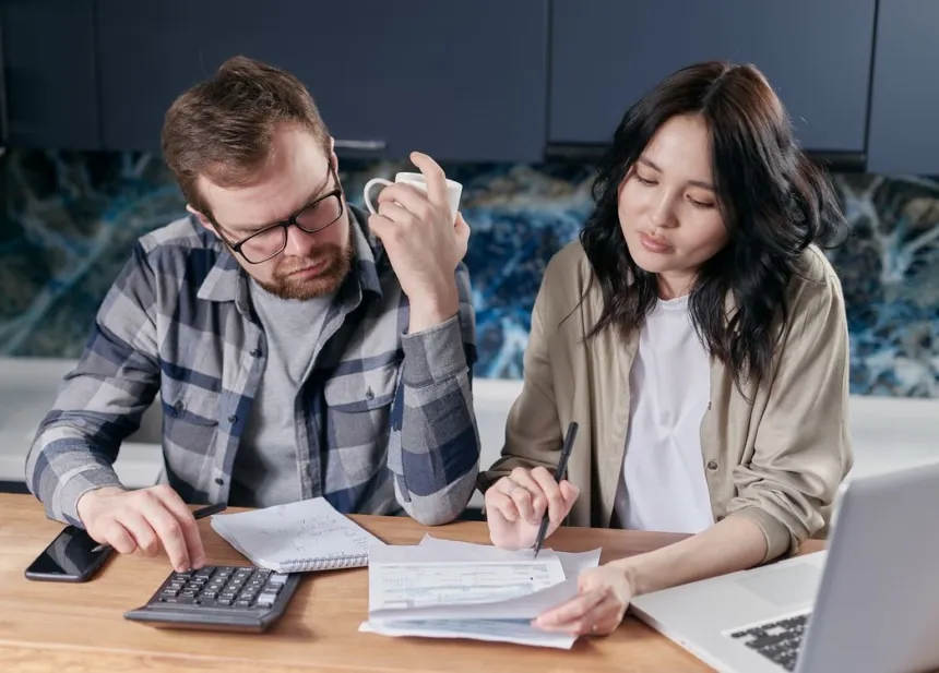 Una pareja revisa facturas y hace cuentas con una calculadora en su casa