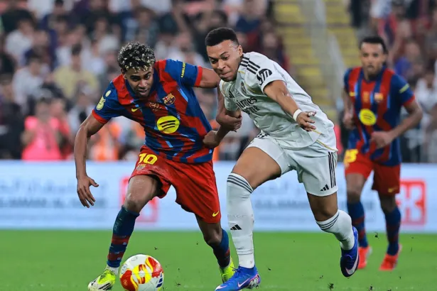 Un jugador del Barcelona y uno del Real Madrid disputan la pelota en la cancha.