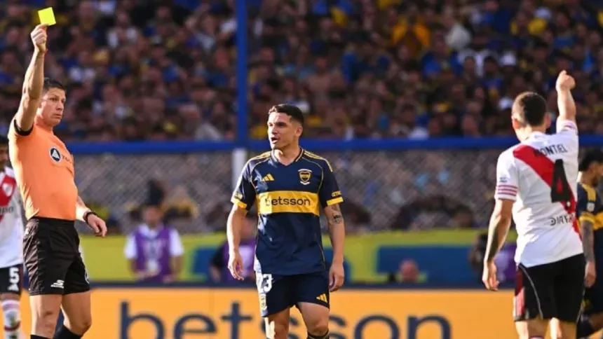 Un árbitro levanta una tarjeta amarilla entre jugadores de Boca y River.