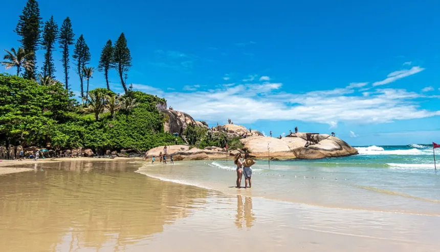 Playa de arena y mar en Brasil, con bañistas y rocas.