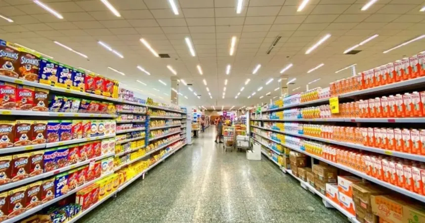 Góndolas de alimentos en un supermercado y una persona comprando al fondo.