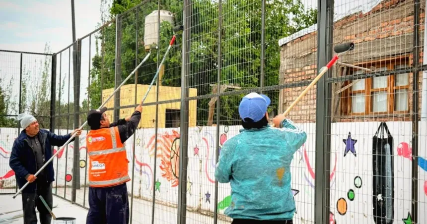 Trabajadores pintan el cercado de una cancha multideportiva.