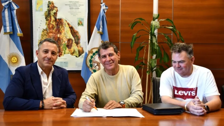 Tres hombres firman un convenio en una oficina con banderas argentinas y de San Juan.