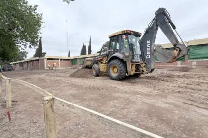 Una retroexcavadora trabaja en el terreno frente a un edificio en refacción.