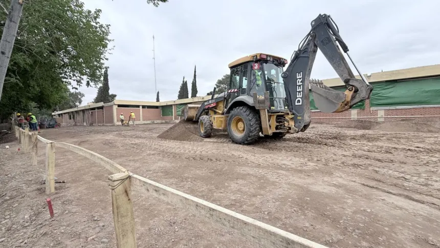 Una retroexcavadora trabaja en el terreno frente a un edificio en refacción.