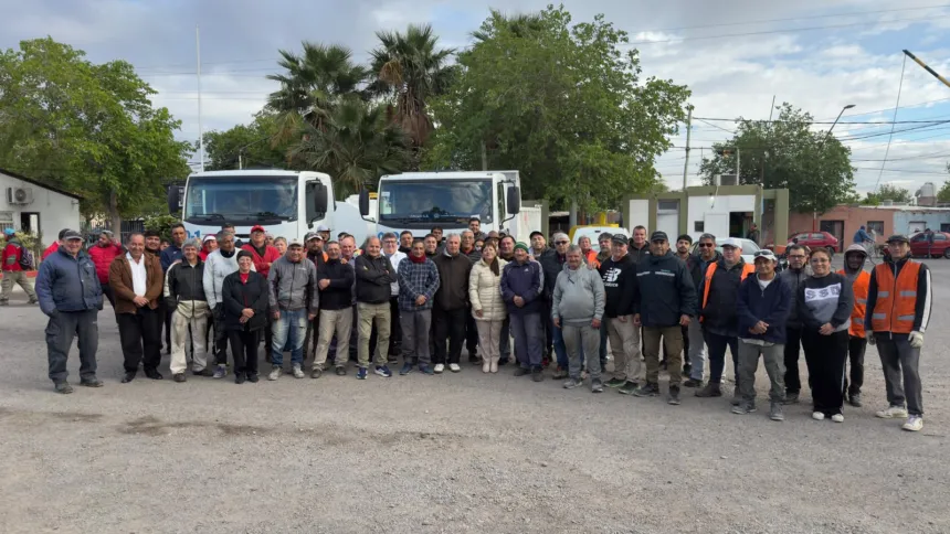 Empleados municipales posan frente a dos camiones.