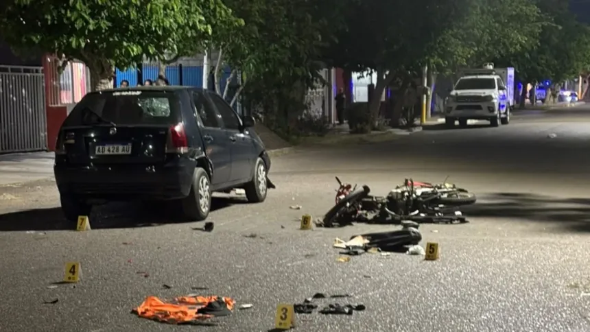 Un auto y una moto dañada en una calle nocturna, con restos y marcadores de evidencia.