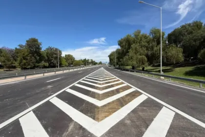 Avenida con demarcación blanca reciente, árboles a los costados y cielo despejado.