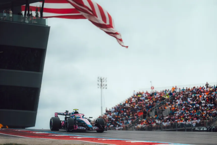 Un auto de Alpine pasa por la pista ante las tribunas y una bandera estadounidense.