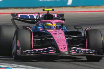 Un auto de Fórmula 1 rosa y azul toma una curva en el circuito.