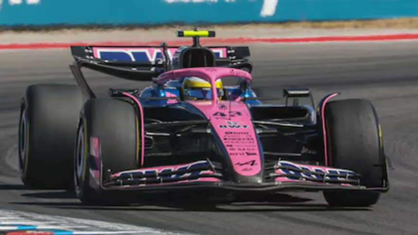 Un auto de Fórmula 1 rosa y azul toma una curva en el circuito.