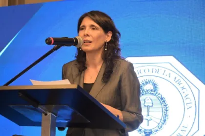 Una mujer adulta habla desde un atril ante el emblema de un colegio de abogados.
