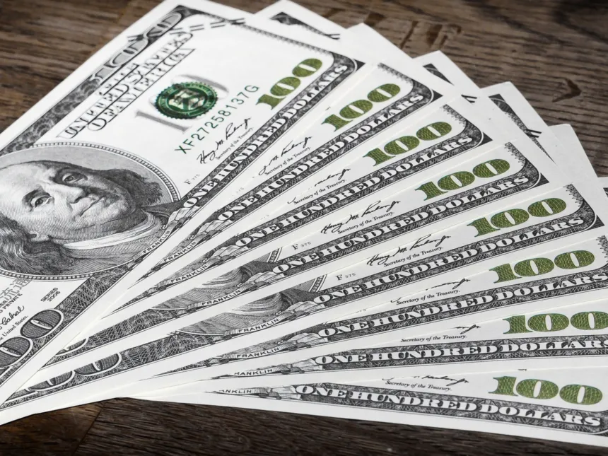 Billetes de cien dólares estadounidenses desplegados sobre una mesa de madera.