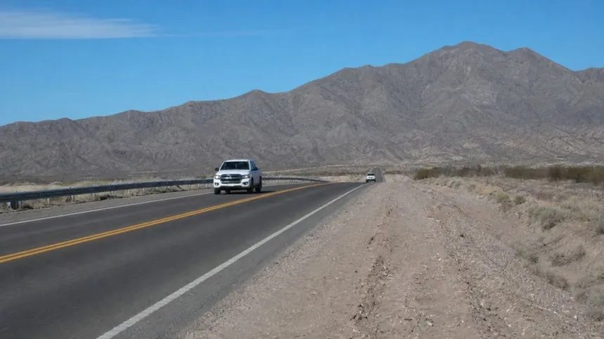 Dos vehículos circulan por una ruta asfaltada entre montañas áridas.