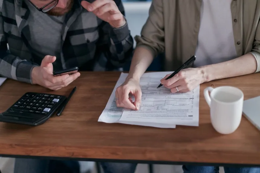 Dos adultos revisan un formulario y hacen cuentas con una calculadora