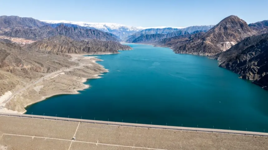 Un dique entre montañas, con agua y amplias franjas de orilla expuesta.
