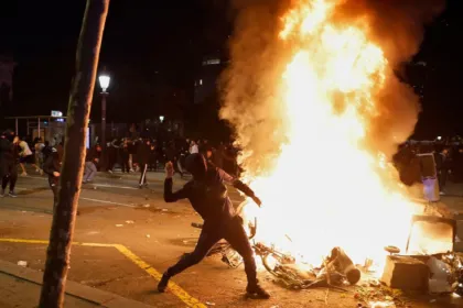 Una persona arroja objetos junto a un gran fuego durante una protesta nocturna.