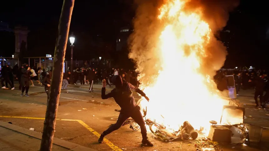 Una persona arroja objetos junto a un gran fuego durante una protesta nocturna.