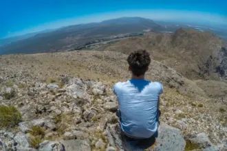 Un joven sentado sobre rocas mira el valle desde lo alto de un cerro en San Juan