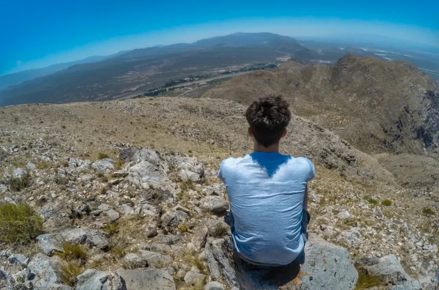Un joven sentado sobre rocas mira el valle desde lo alto de un cerro en San Juan