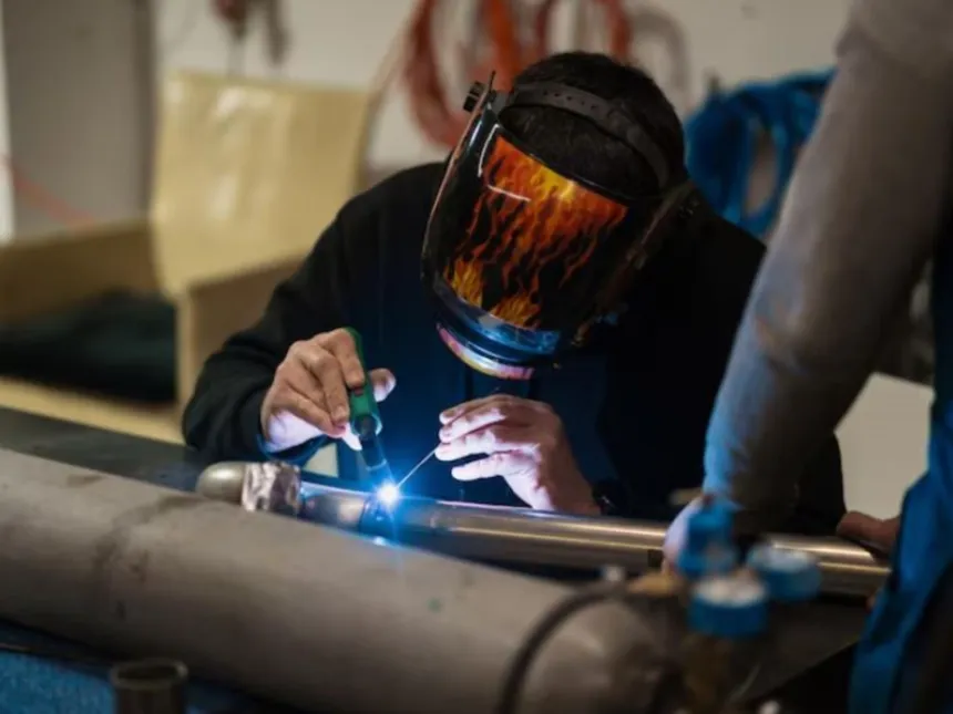 Una persona suelda una pieza metálica en un taller industrial.