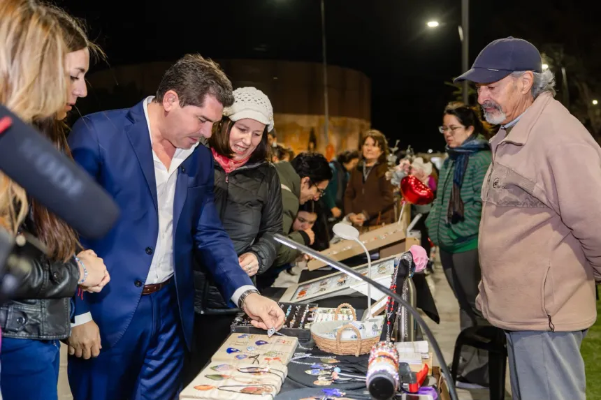 Marcelo Orrego observa artesanías en un puesto de la feria junto a visitantes.