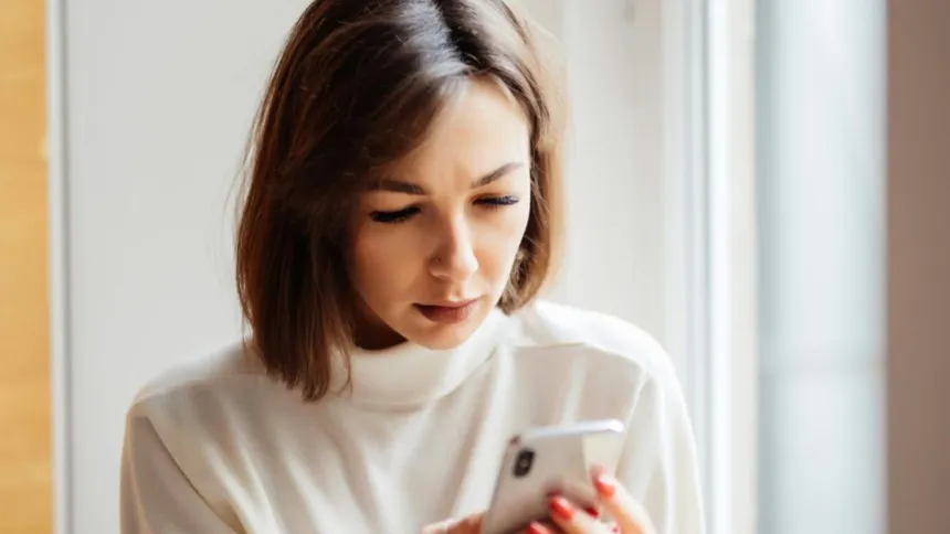 Una mujer adulta mira la pantalla de su celular.