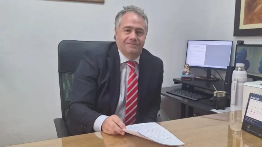 Un hombre con traje sostiene documentos sentado en un escritorio de oficina.