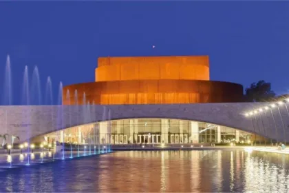 Teatro iluminado de noche, con fuentes y agua en primer plano.