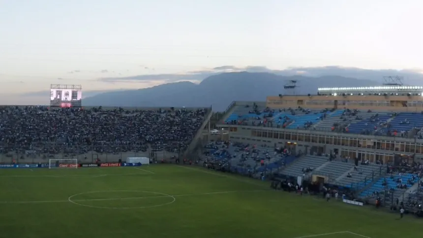 Público en las tribunas del estadio del Bicentenario junto a una cancha de fútbol al atardecer.