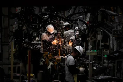 Operarios con cascos trabajan entre chispas en una fábrica.