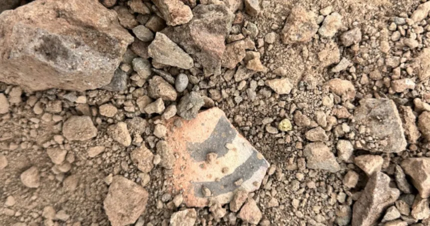 Fragmento cerámico decorado entre piedras en un terreno árido.