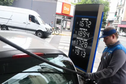 Un empleado carga combustible a un auto junto al cartel de precios de la estación.